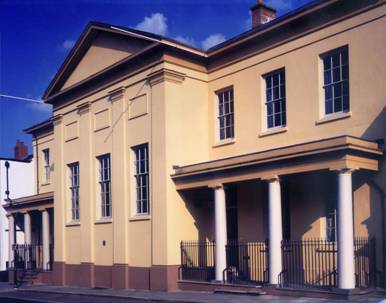 A yellow, two-storey building with tall windows and white columns along the front entrance.