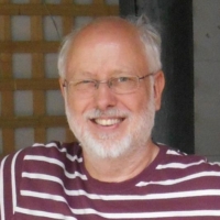 Smiling older man with glasses and a white beard, wearing a maroon and white striped shirt.