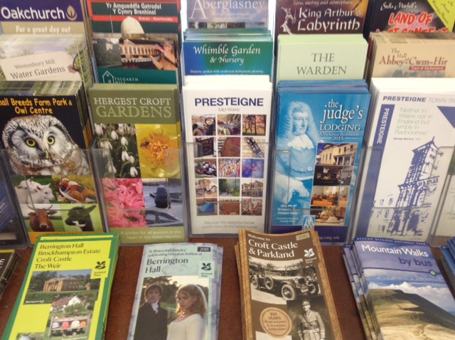 A display of colourful tourist brochures for local attractions and gardens, arranged upright on a counter.