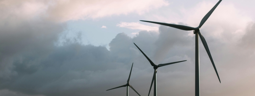 Three wind turbines stand on grassy land under a cloudy sky with sunlight breaking through.